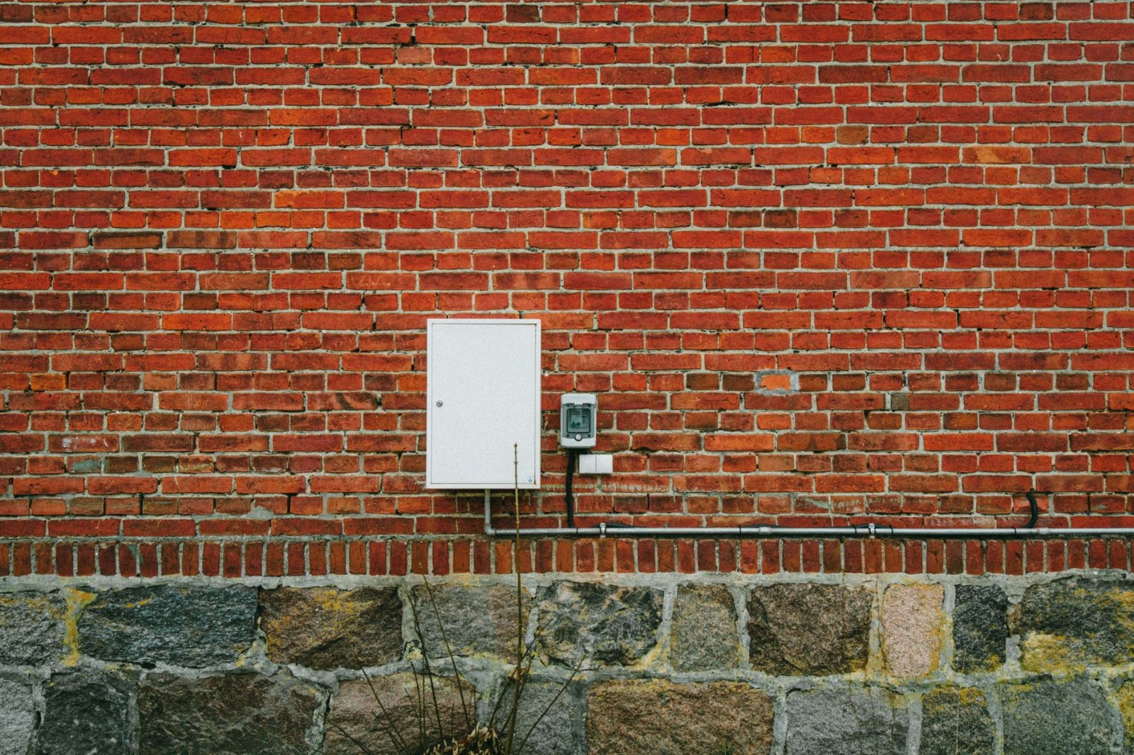 The exterior half of the same kind of job: an installed meter set on common brick with its riser conduit strapped and terminated down to grade, cover on and sealed.